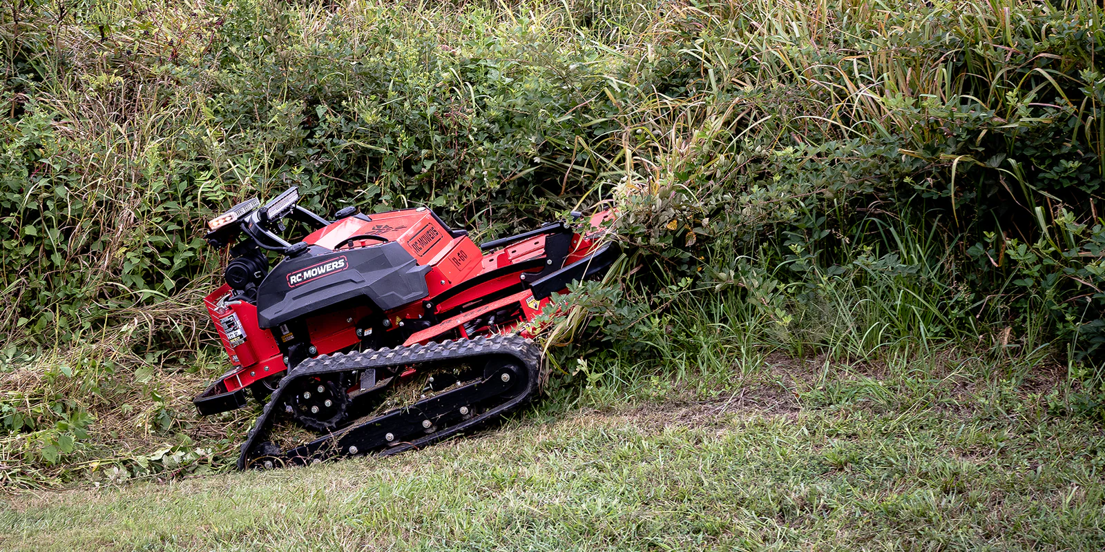 Red robotic mower trimming overgrown grassy field