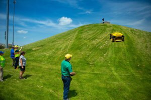 People watching remote-controlled mower on grassy hill